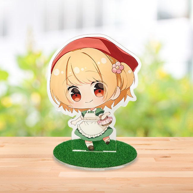 木目調テーブルに置かれた赤ずきんの女の子の芝生台座アクスタ。緑豊かなボケた背景。